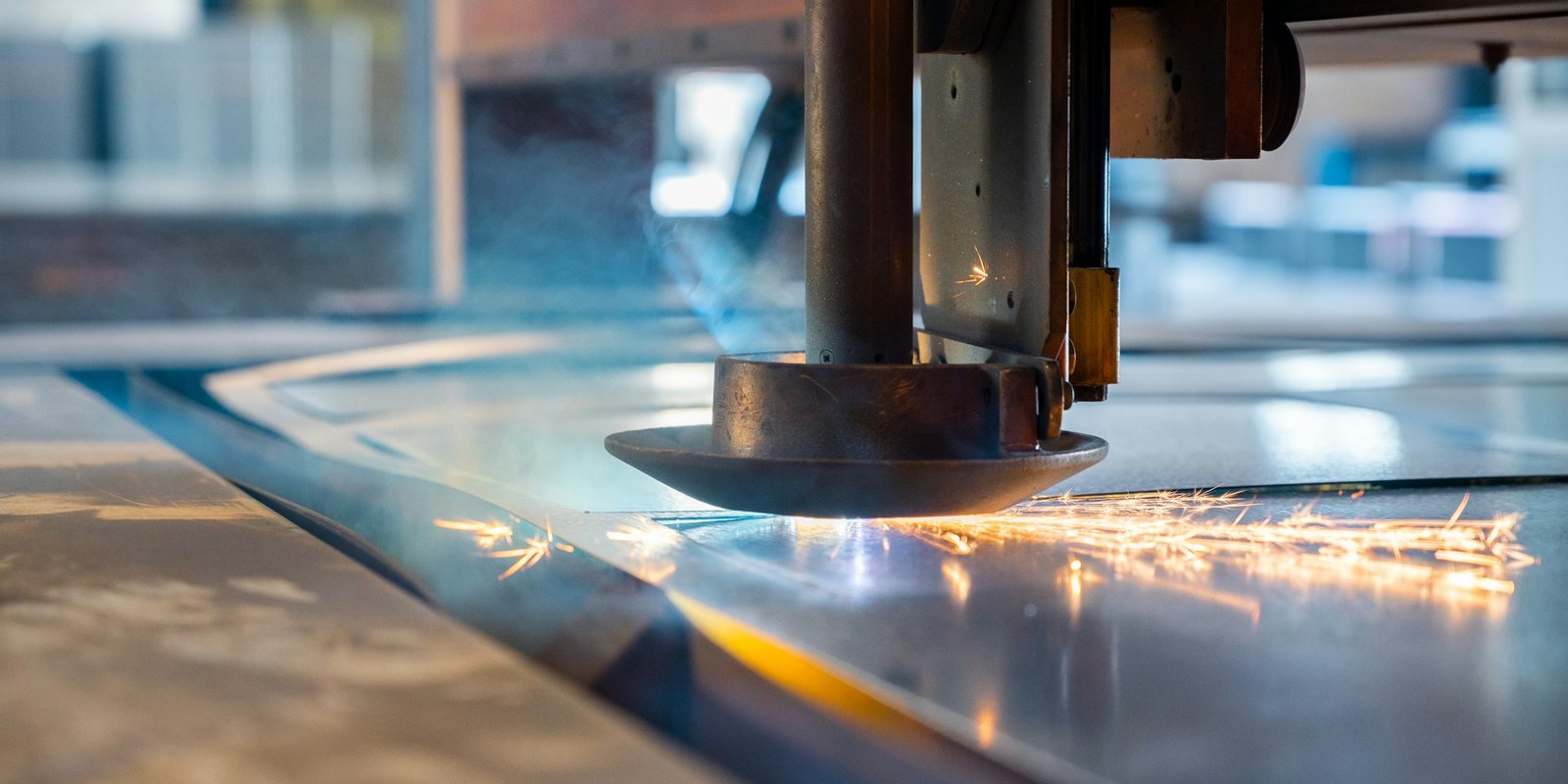 A cutting head moves over a steel sheet on a CNC cutting machine, throwing a thin line of sparks