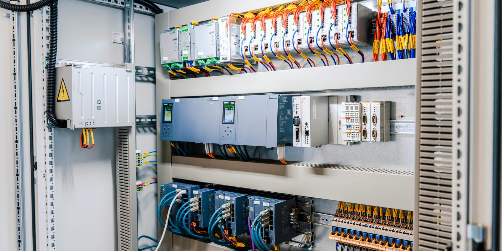 Open industrial control cabinet with PLC modules, network switches and neatly labelled wiring on DIN rails