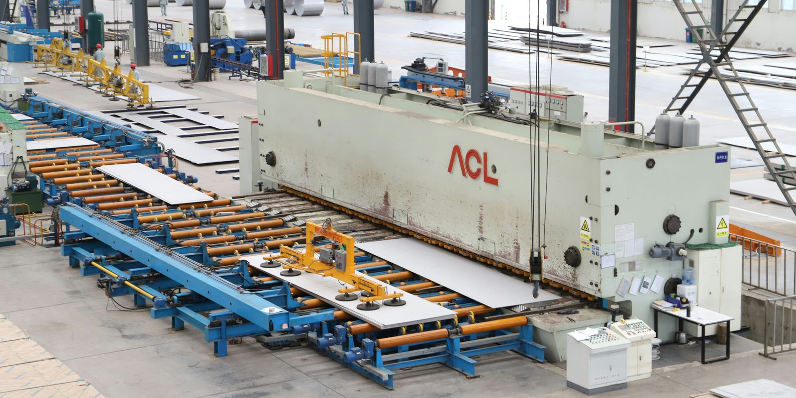 A large shearing machine and roller table cut metal sheets in a bright, spacious factory hall