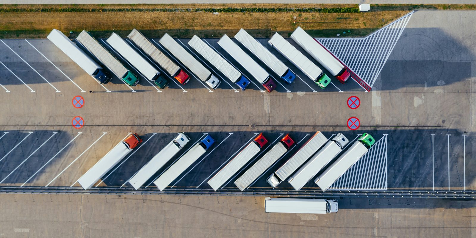 Aerial view of transport trucks with white trailers parked at an angle in two rows on a truck lot