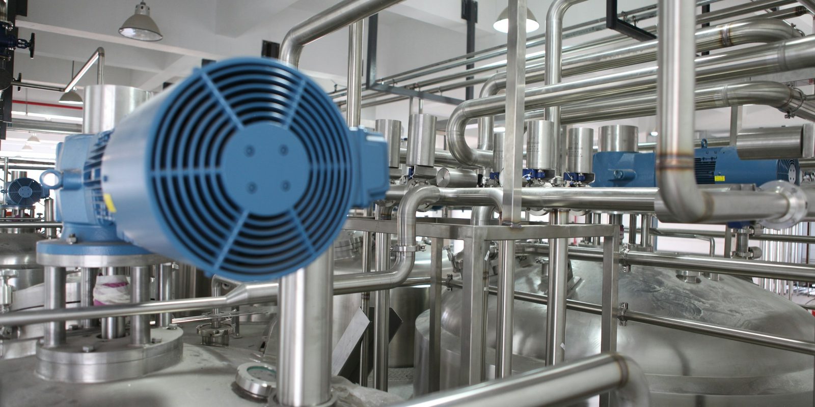 Stainless steel process piping and tanks with a blue motor in a clean, brightly lit production plant