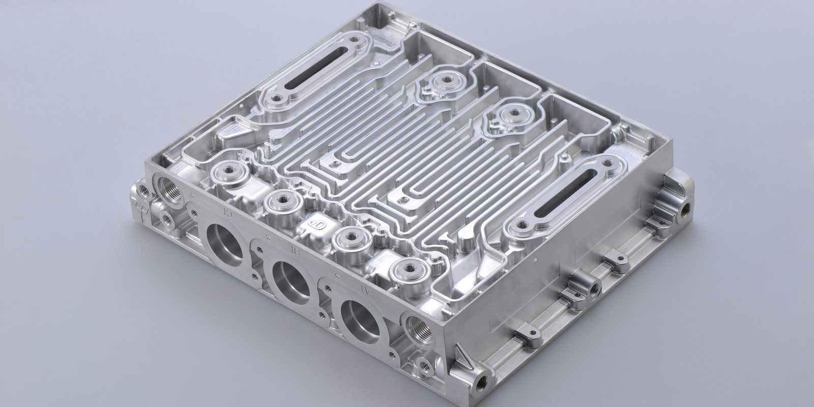 A precision-machined aluminium housing with milled channels and threaded ports, on a light grey background