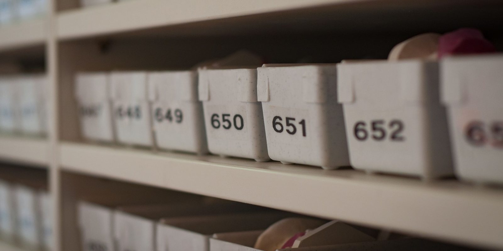 White plastic bins on a shelf, each marked with a printed number, such as 650, 651 and 652