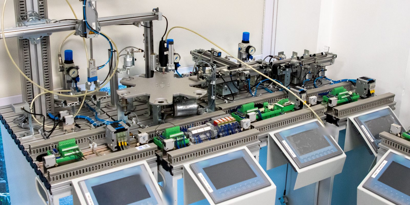 Row of automation training stations with pneumatic modules and HMI touchscreens in a bright white lab