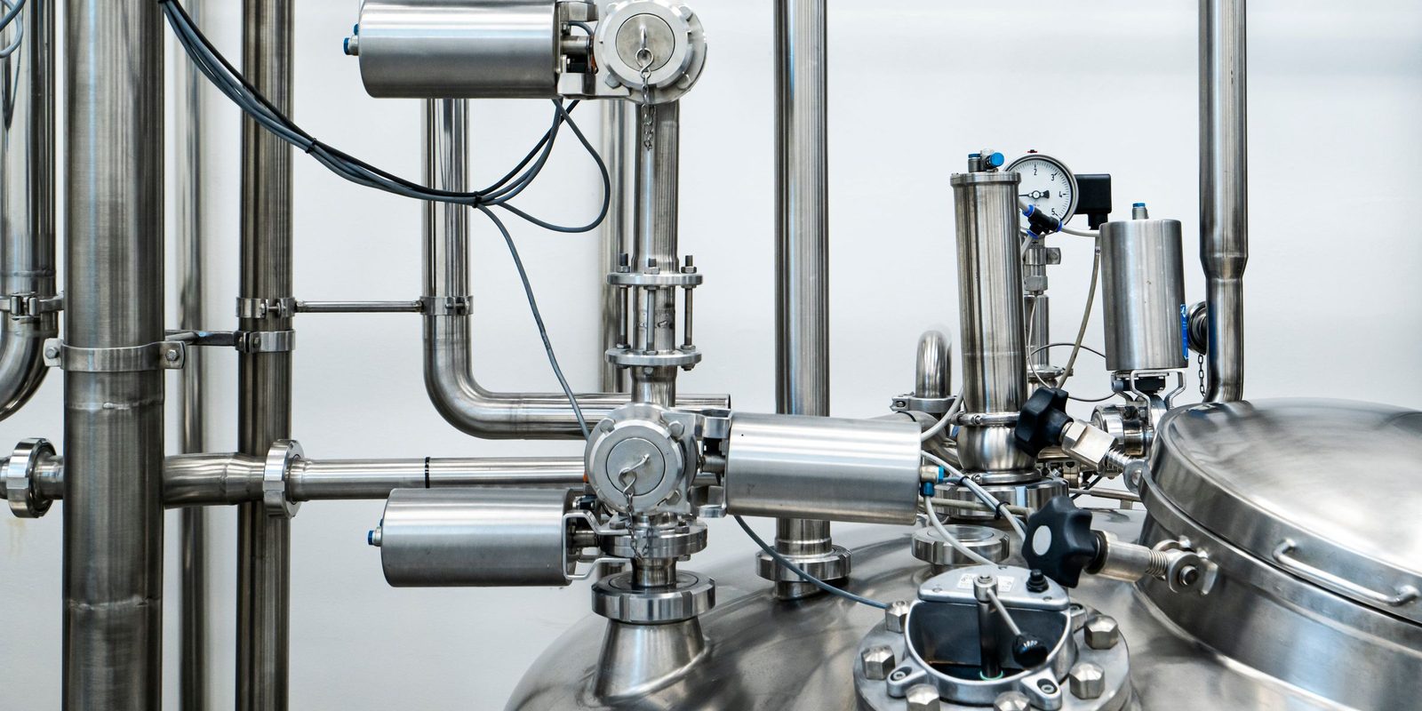 Stainless steel valves, piping and a pressure gauge on top of a process tank in a bright plant