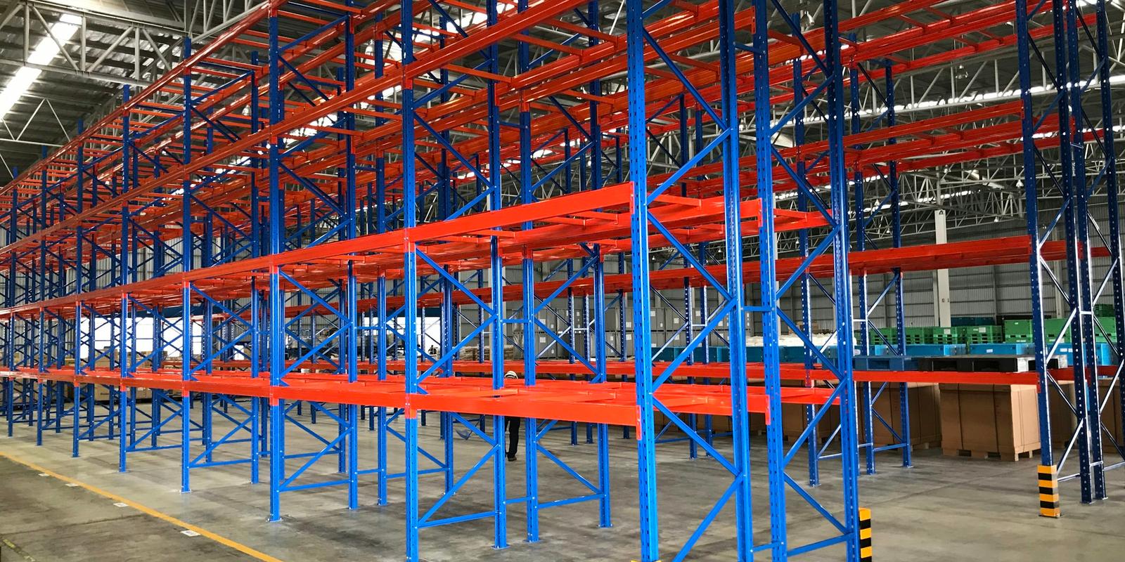 Rows of empty blue and orange pallet racks in a bright, newly built warehouse