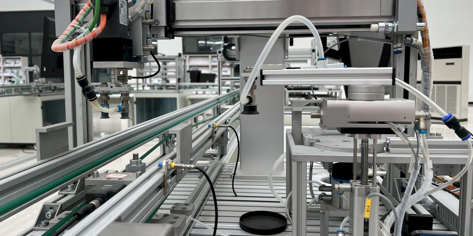 Pick-and-place gantry with vacuum grippers above a conveyor on a bright, clean automated assembly station