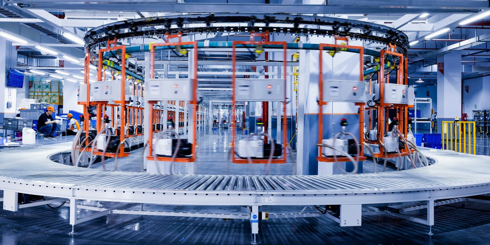 Circular automated inspection line with orange test frames above a roller conveyor on a bright plant floor