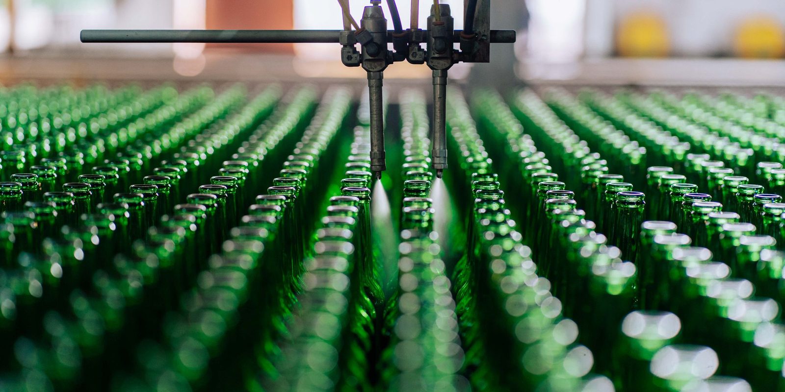 Rows of green glass bottles move along an automated line under a set of filling nozzles