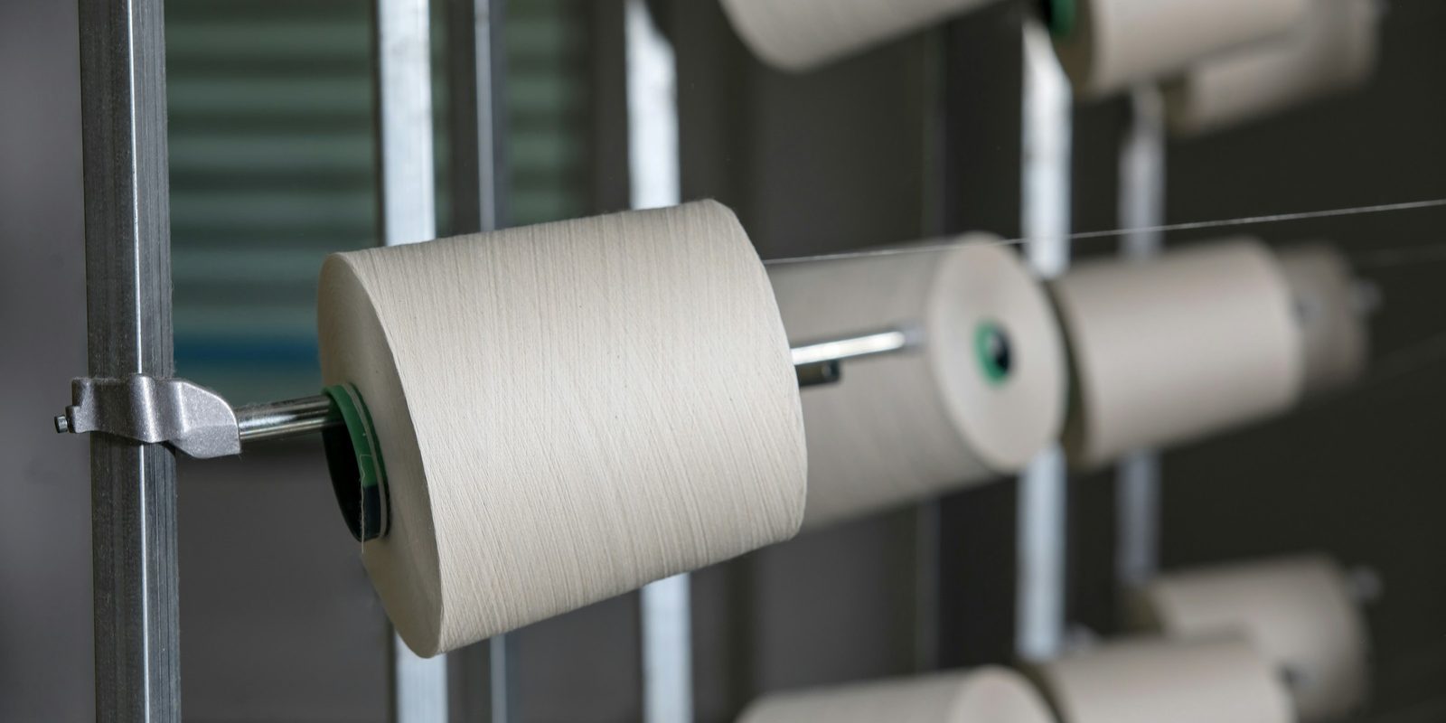 White yarn cones sit on steel spindles on a textile machine