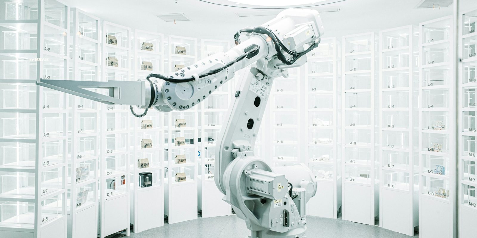 A white industrial robot arm stands in a round white room lined with numbered glass storage cabinets