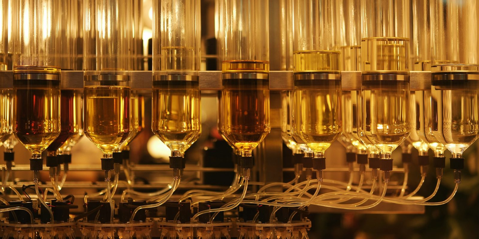 Glass reservoirs of amber liquid feed a row of nozzles and tubes on a mixing machine