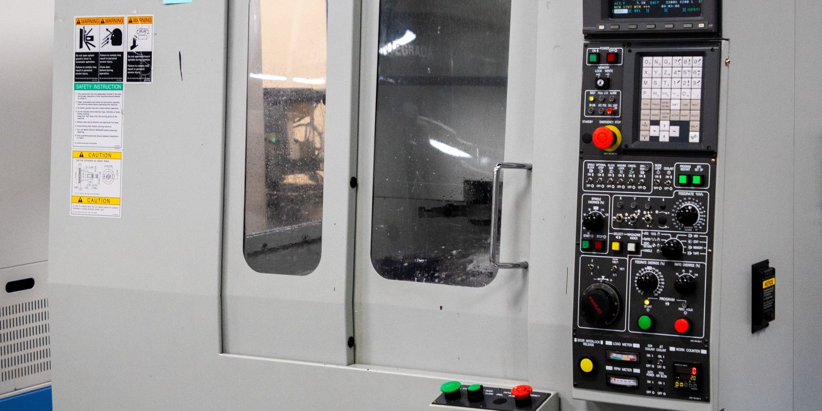 The front of a white CNC vertical machining centre, door closed, with its control panel, keypad and spindle controls on the right