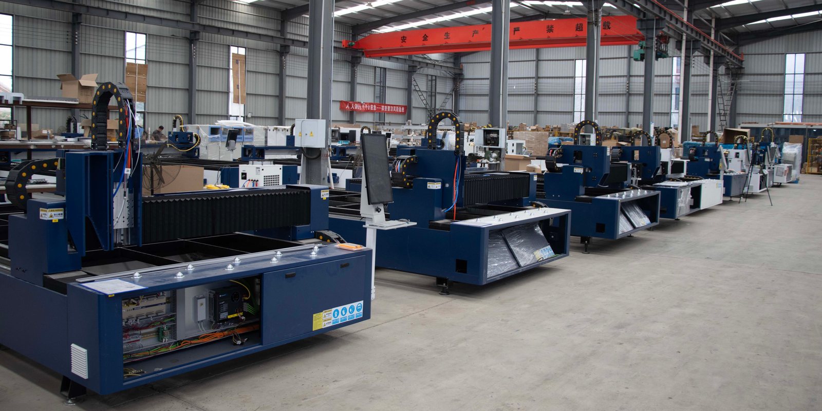 A row of new blue laser cutting machines on the clean floor of a bright, high-ceilinged factory hall