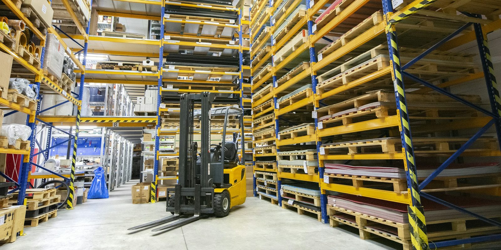 Sheets of raw material on pallet racks and a forklift in a bright, orderly stockroom