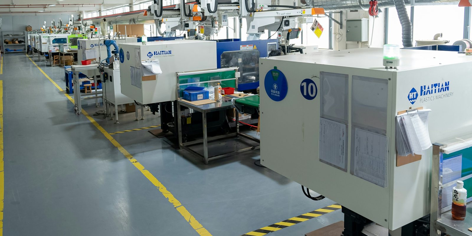 A clean, brightly lit production hall with a row of white moulding machines along a yellow-marked aisle