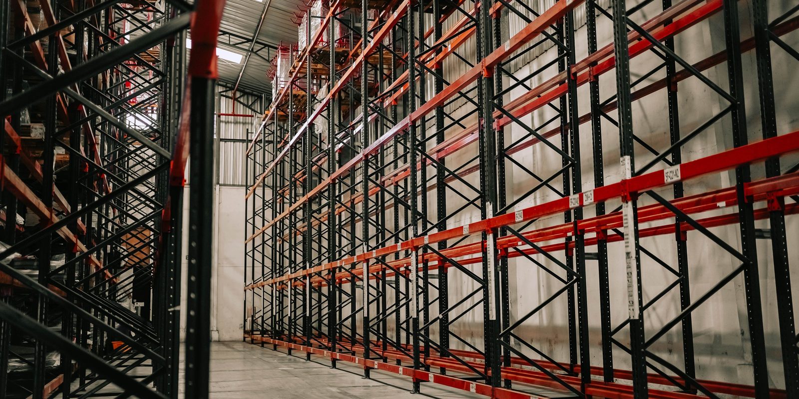 Tall steel pallet racking with red beams and dark green uprights, still empty, in a clean, high-ceilinged warehouse