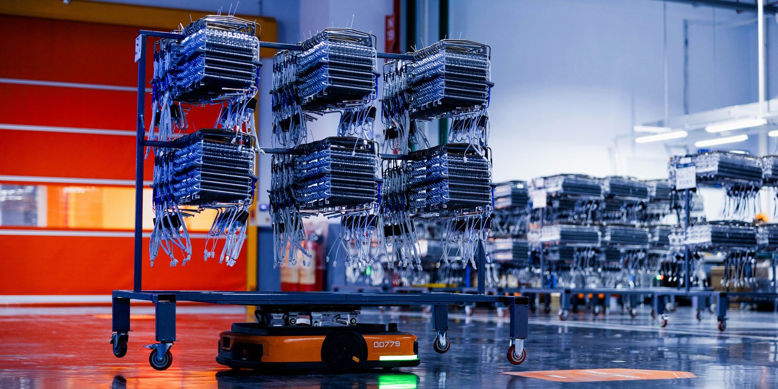 An automated guided vehicle carries a rack of parts across a clean, bright plant floor