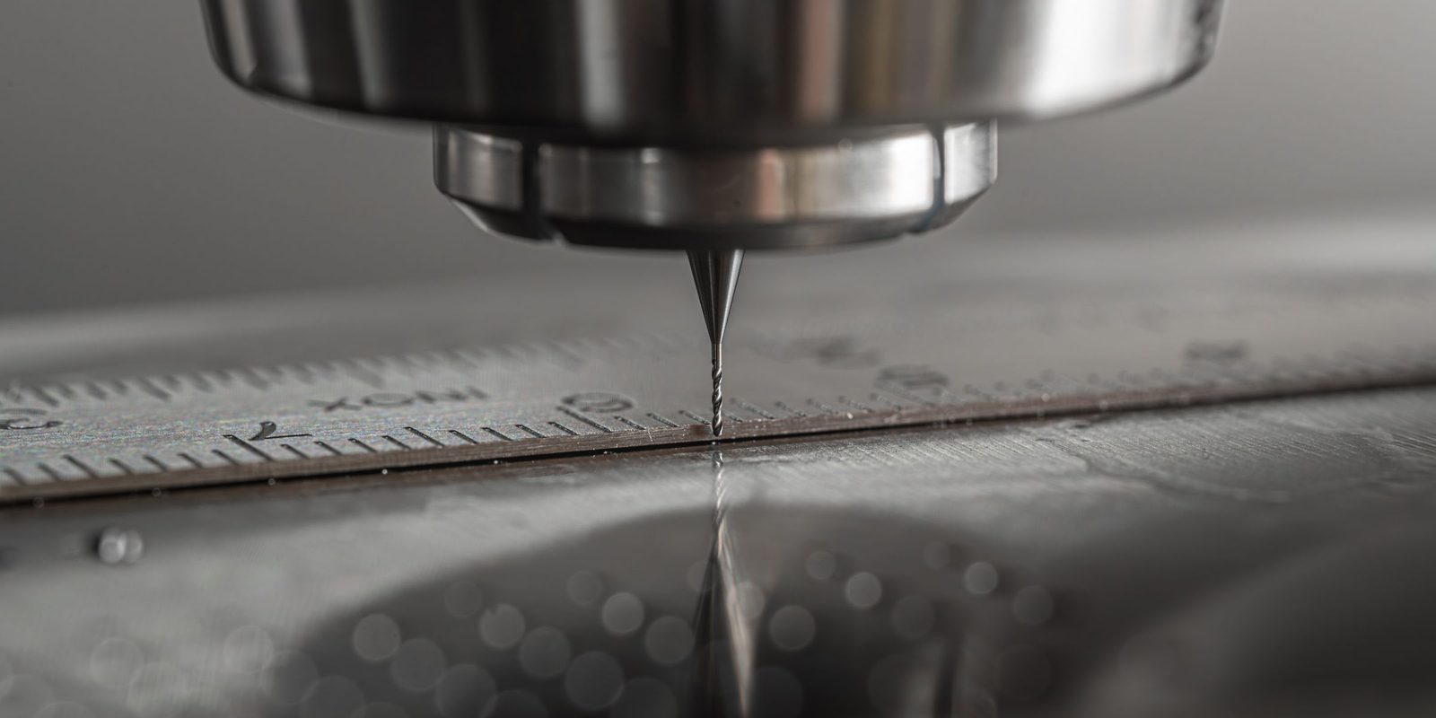 A fine engraving tool held a hair above a stainless steel rule under a CNC spindle