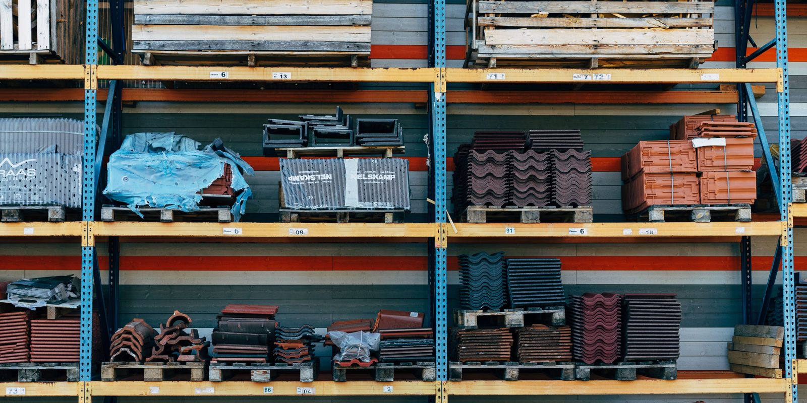 Steel pallet racks with yellow beams holding stacked roof tiles, panels and bagged materials in a tidy warehouse