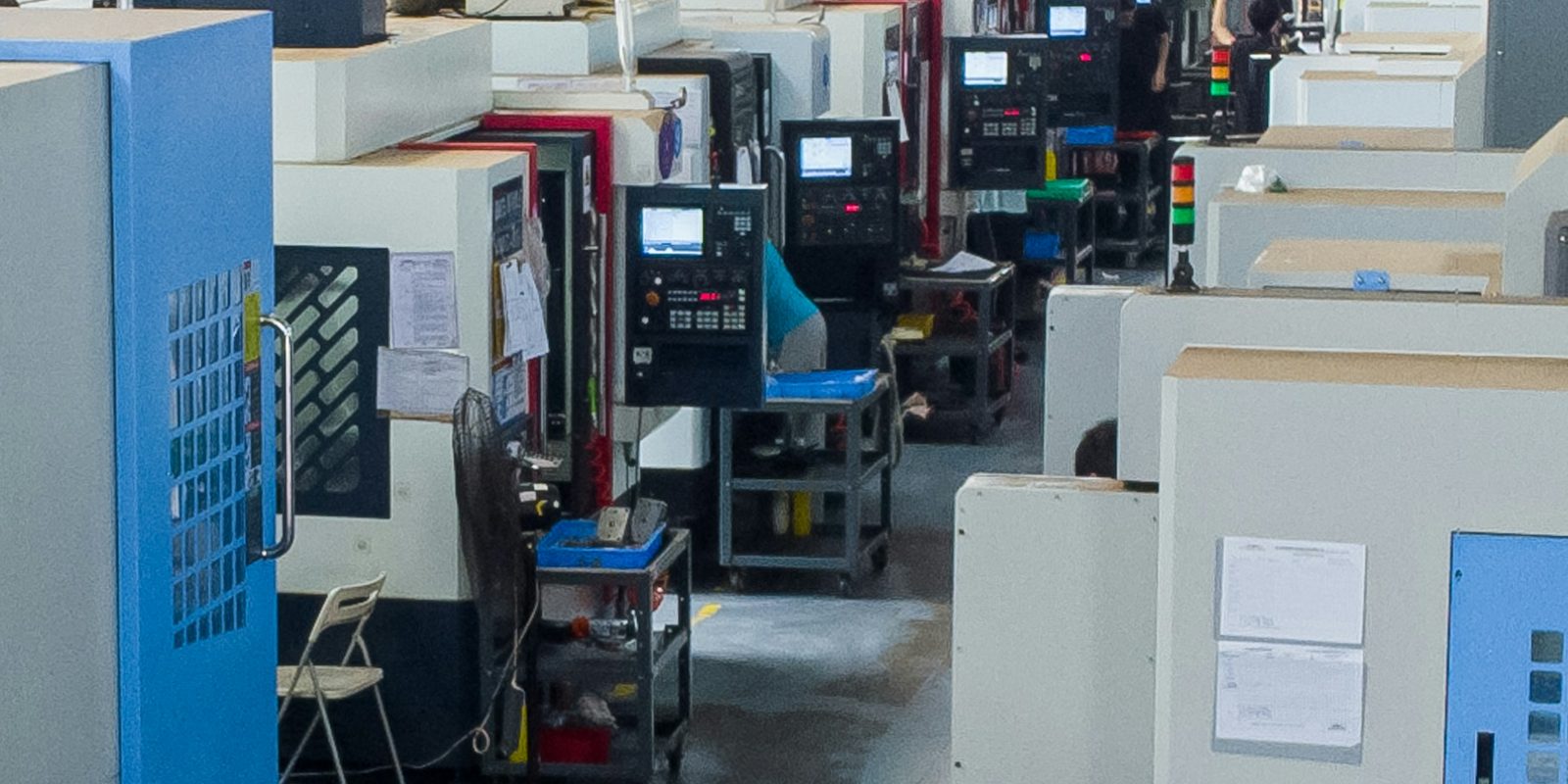 A row of CNC machining centres with lit control screens along an aisle in a bright machine shop
