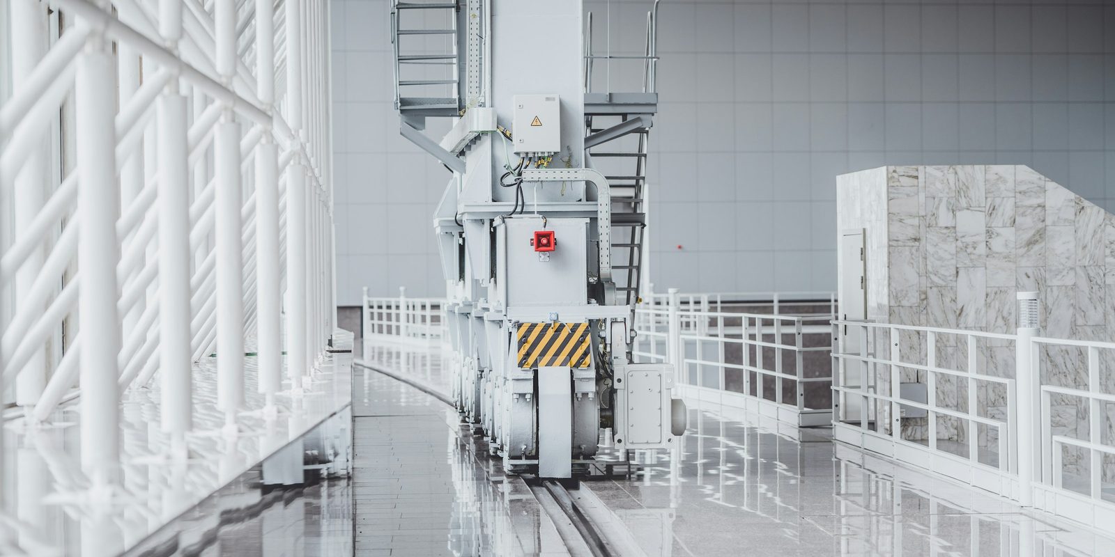 A white automated machine on rails in a bright production hall with white railings and a polished floor