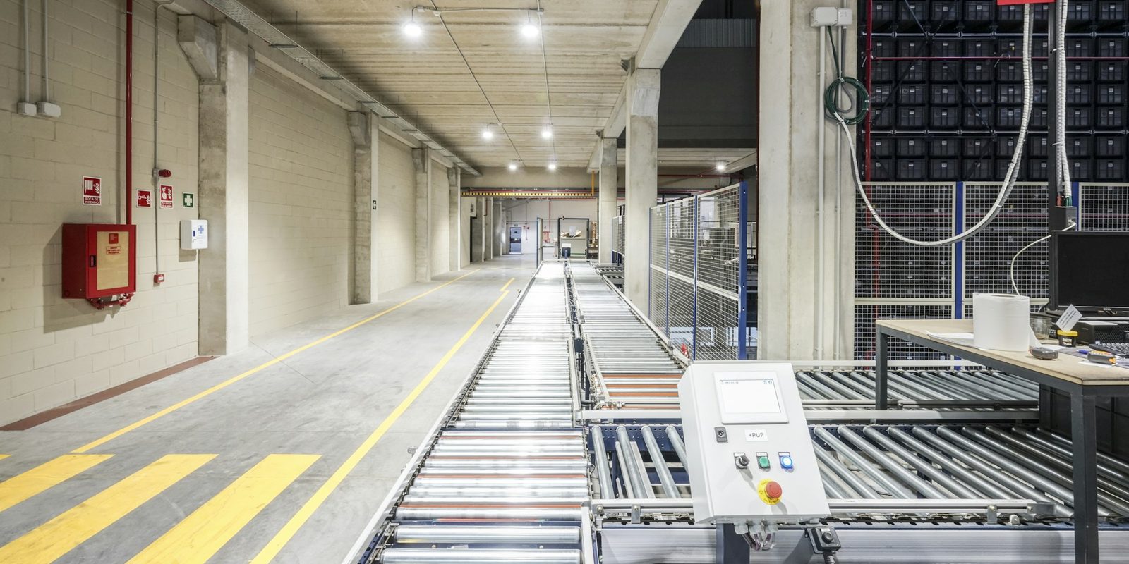 Roller conveyors run through a bright, clean automated line past a control station with a touchscreen and an emergency stop