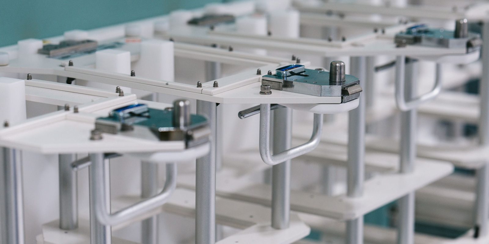 Close-up of rows of identical white equipment stands with metal clamps and handles, repeated in a clean, bright workspace