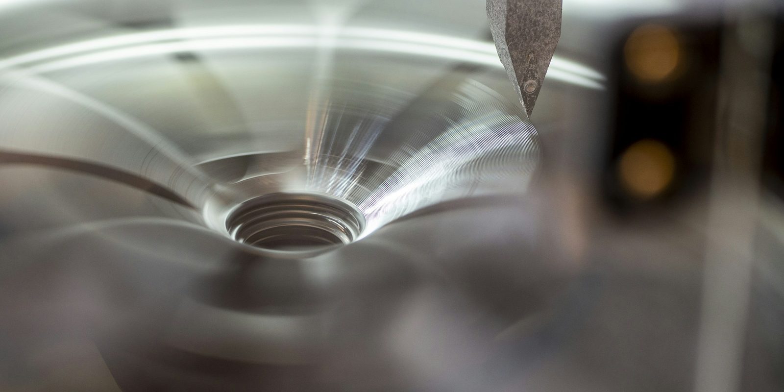 Close-up of a cutting tool against a spinning metal part, leaving fine circular tool marks around a center hole