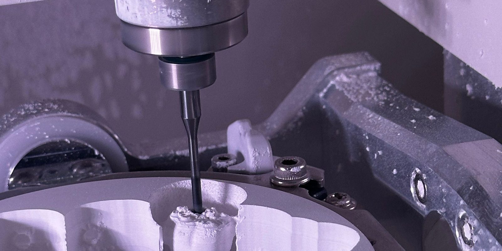 A thin end mill in a CNC milling machine cuts a small part out of a white disc-shaped blank