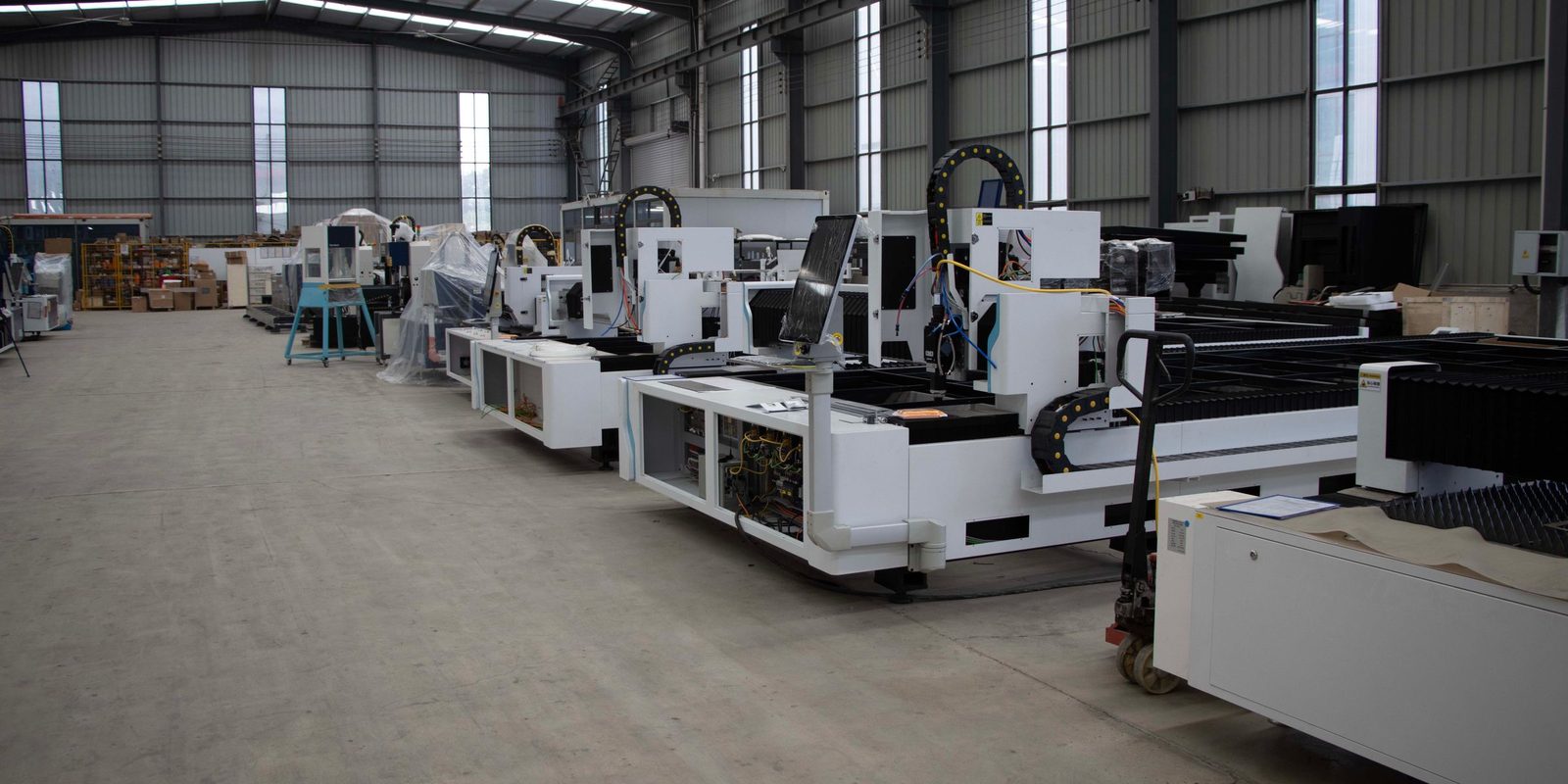 A row of white industrial cutting machines in a bright, high-roofed factory hall