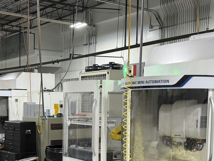 A row of white CNC tool grinding machines with glass doors and control panels in a bright machine shop