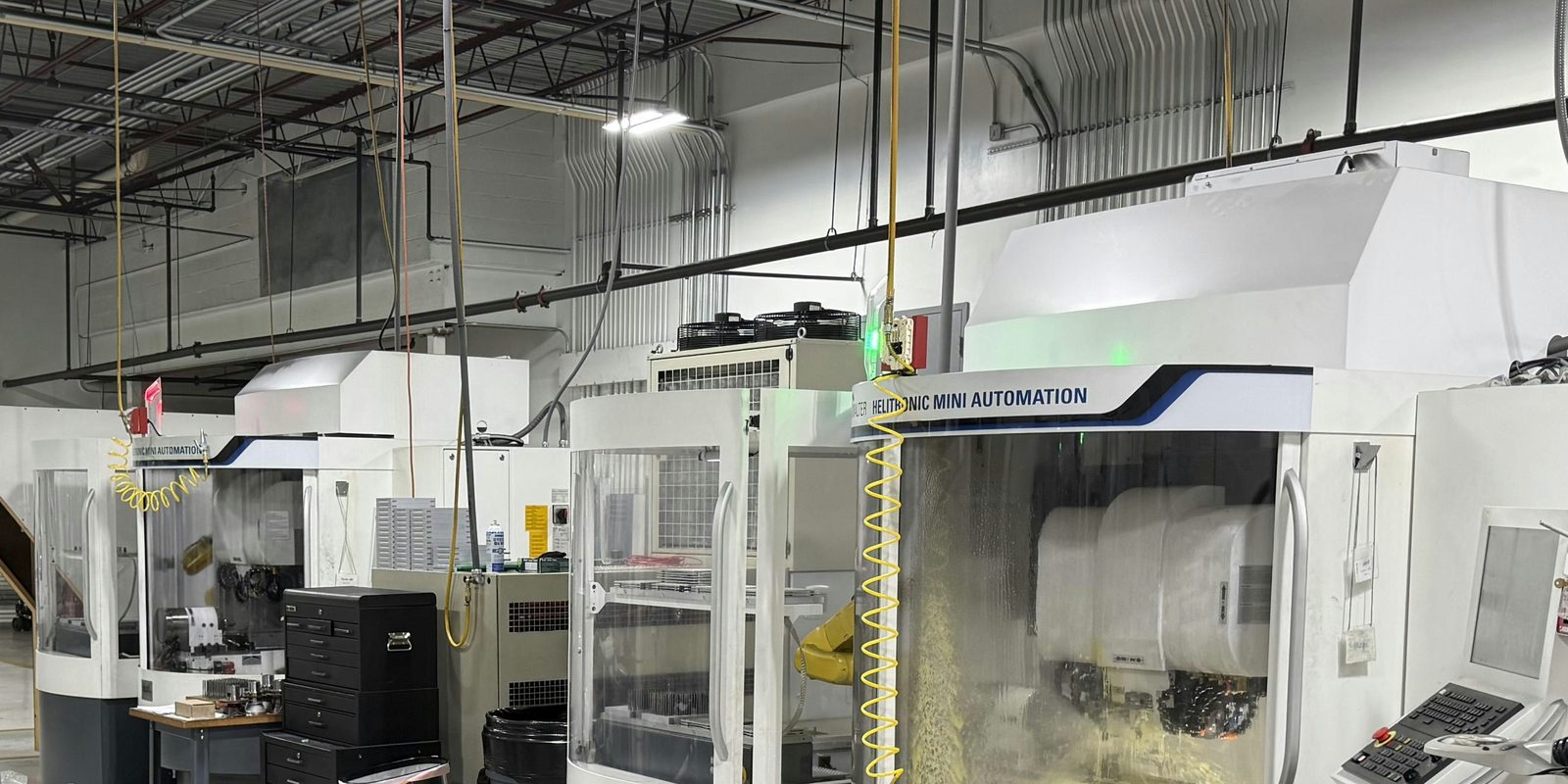 A row of white CNC tool grinding machines with glass doors and control panels in a bright machine shop