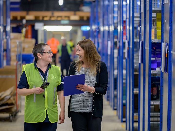 Two warehouse employees in an aisle of blue shelving, one with a handheld scanner