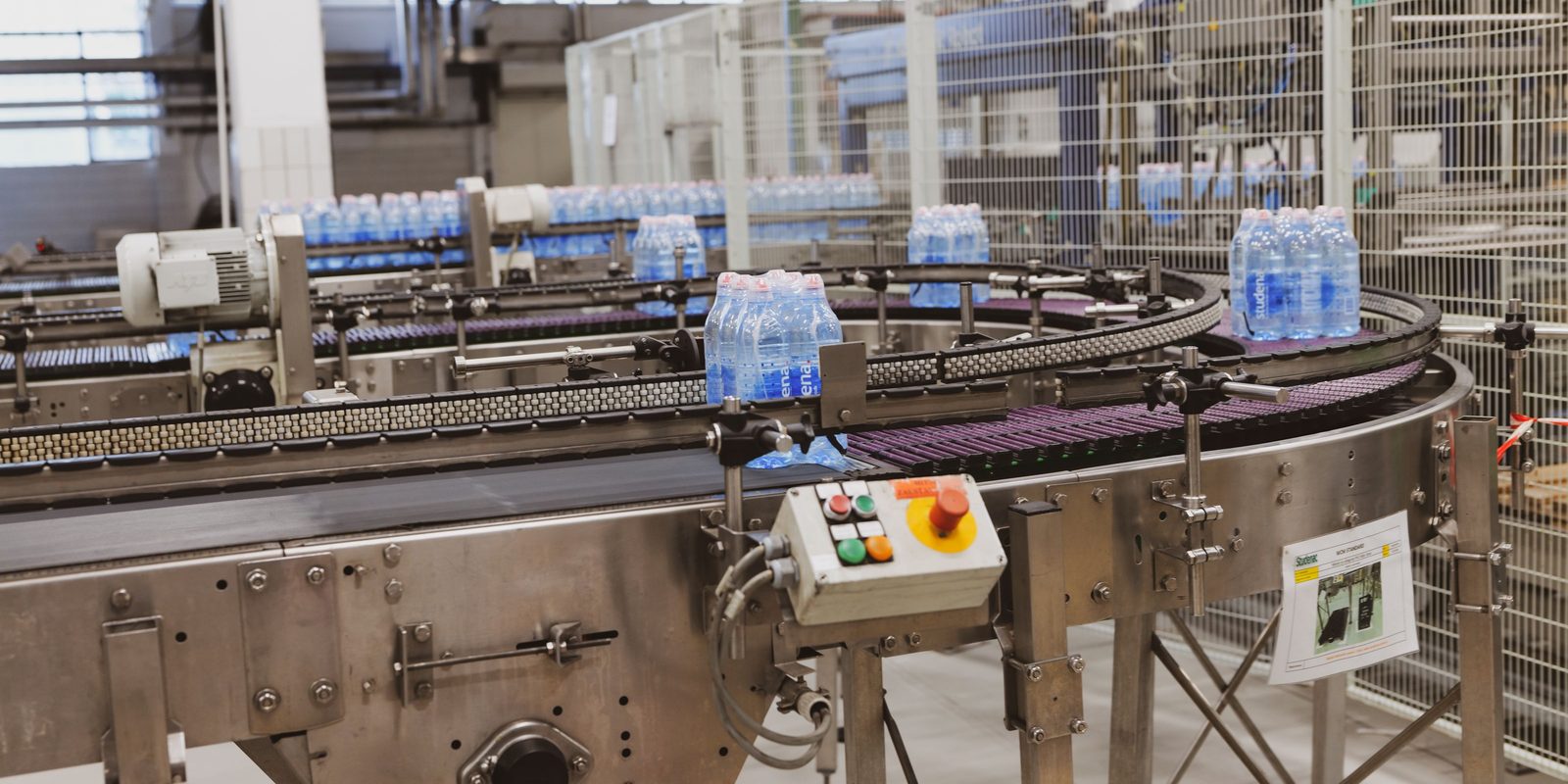 Shrink-wrapped packs of bottled water moving along a curved conveyor in a bright bottling plant