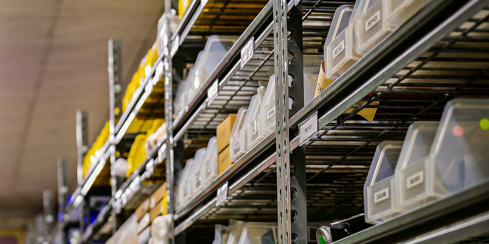 Clear plastic bins on wire shelving in a stockroom, each bin with a printed label