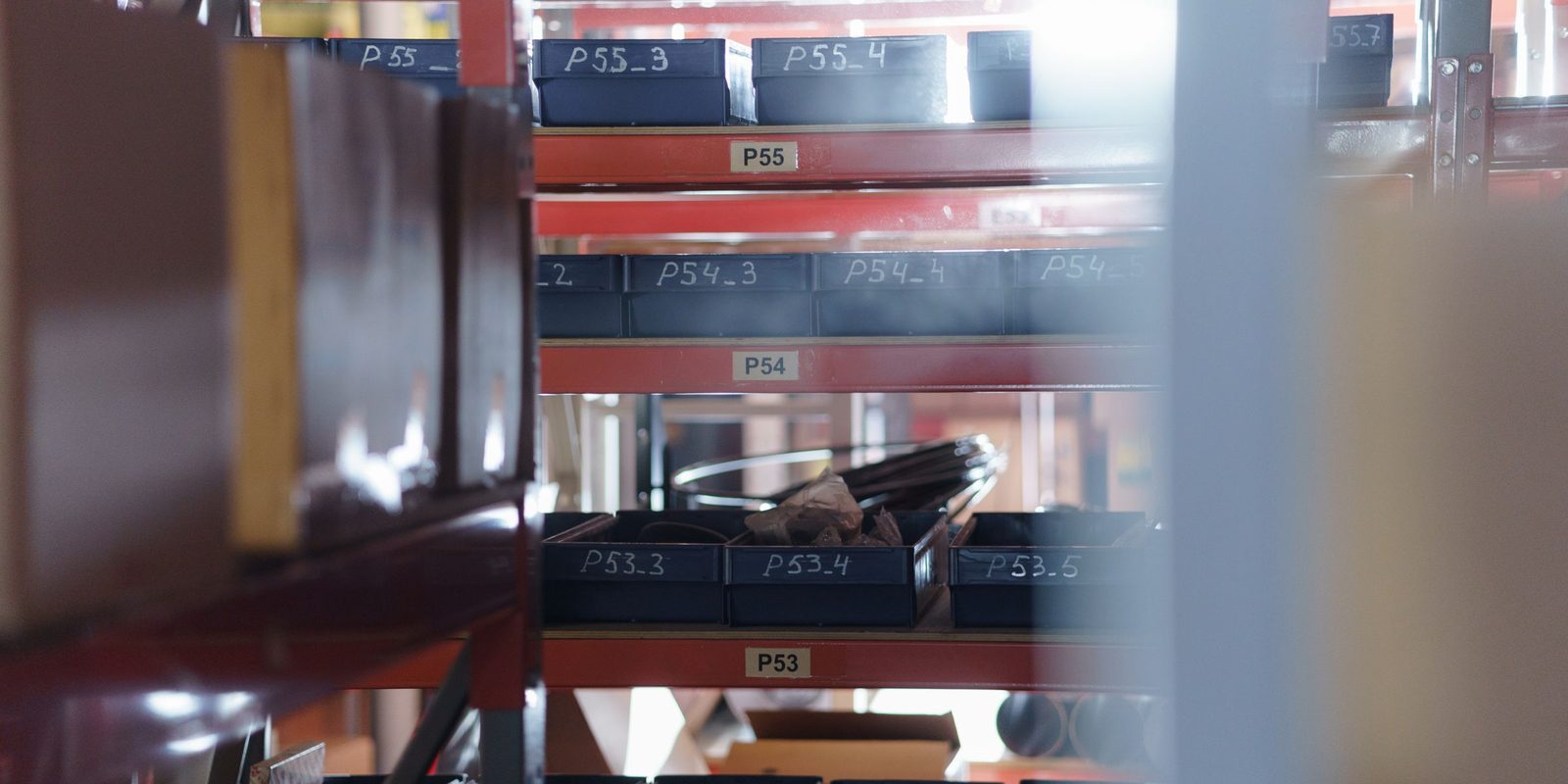 Dark storage trays on red shelving, each tray marked with a location code such as P53_3 or P54_4