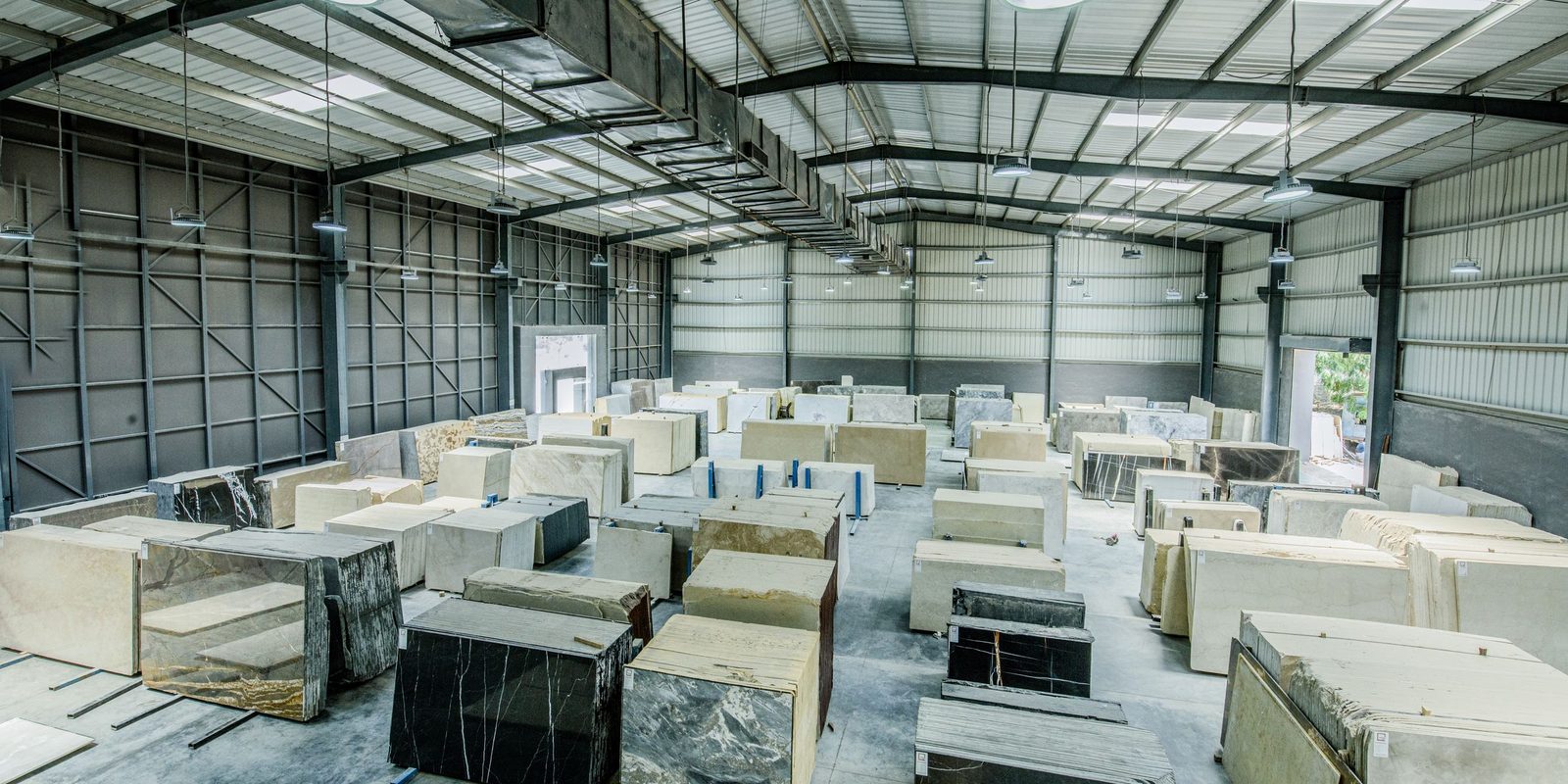 Rows of stone slabs in a bright steel-frame warehouse, each slab with a small tag