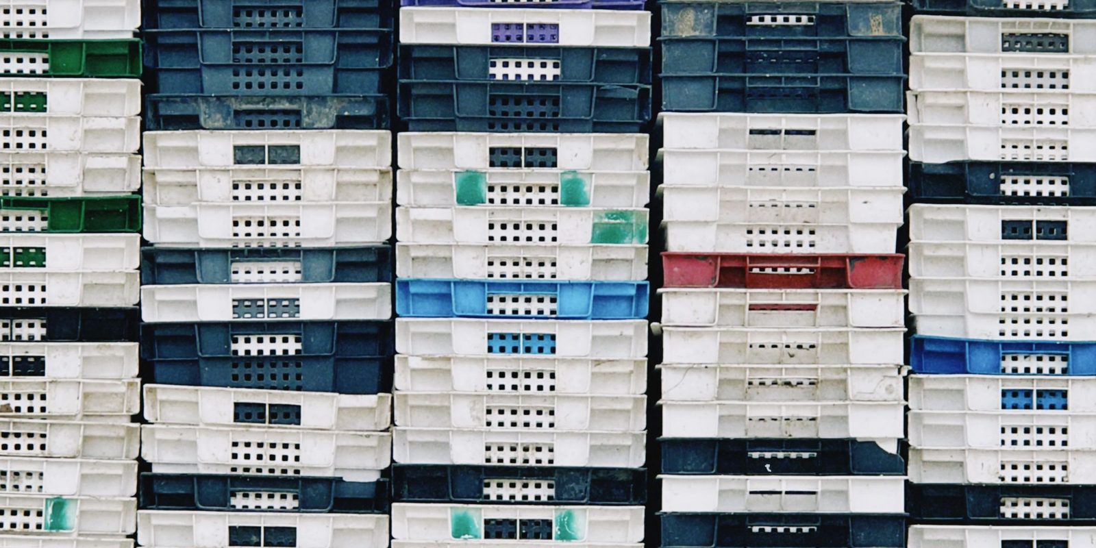 Stacks of white, dark blue and green plastic crates against a warehouse wall