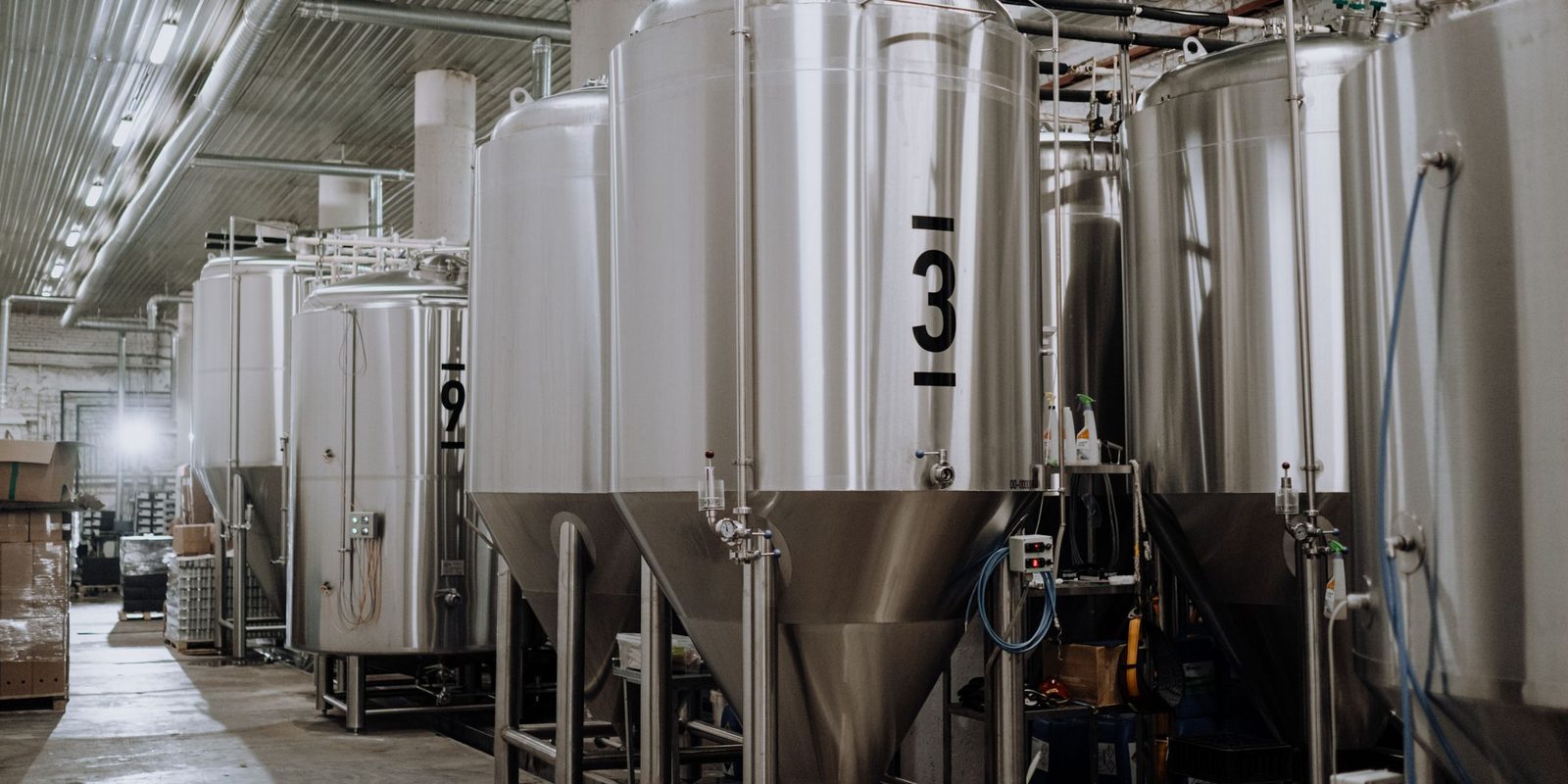 Stainless steel tanks numbered 3 and 9 on a production floor, with pallets of boxed stock in the aisle