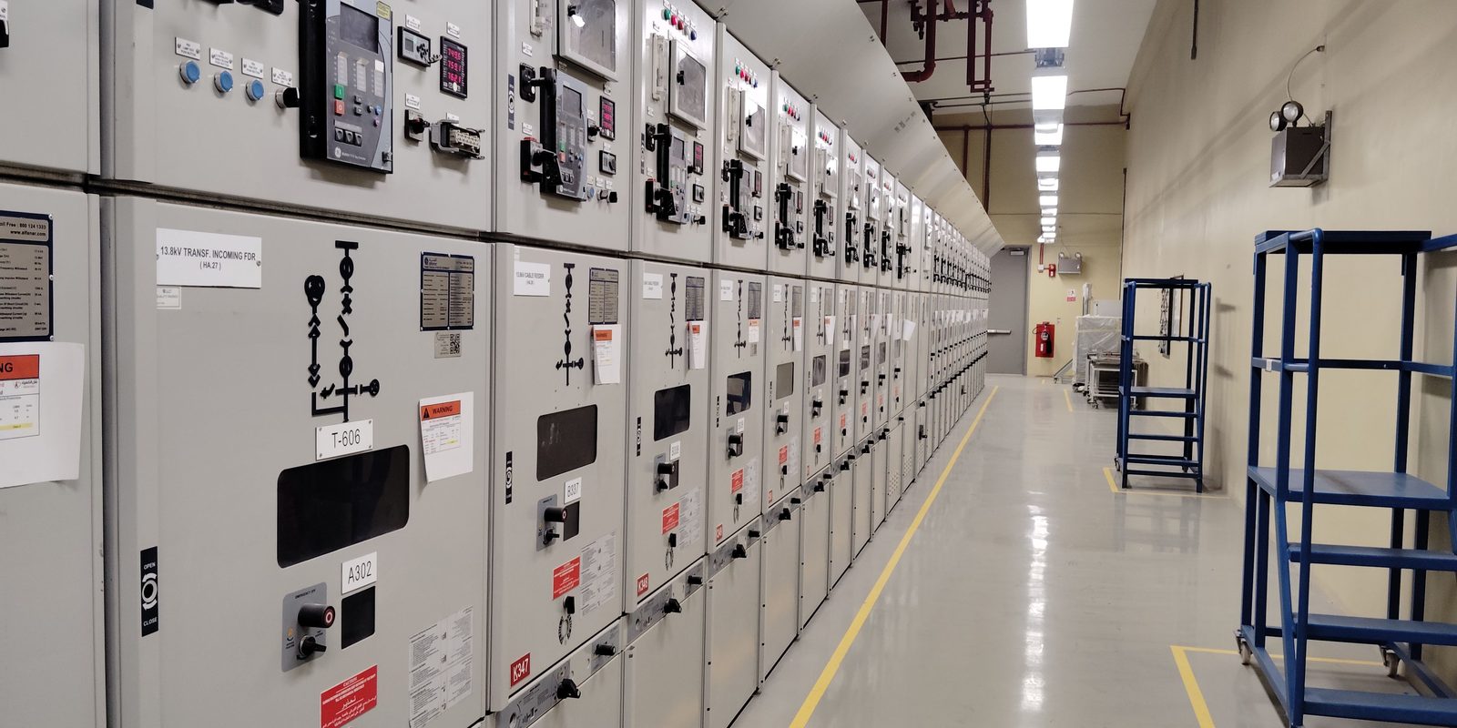 A long row of grey electrical switchgear cabinets with control panels along a clean, brightly lit electrical room