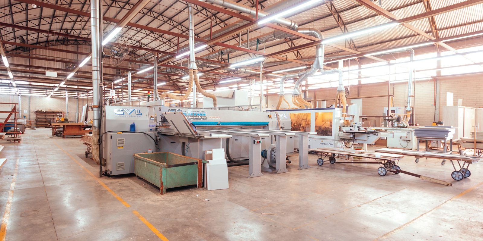 A bright, tidy factory floor with panel processing machines under a high steel roof and skylights
