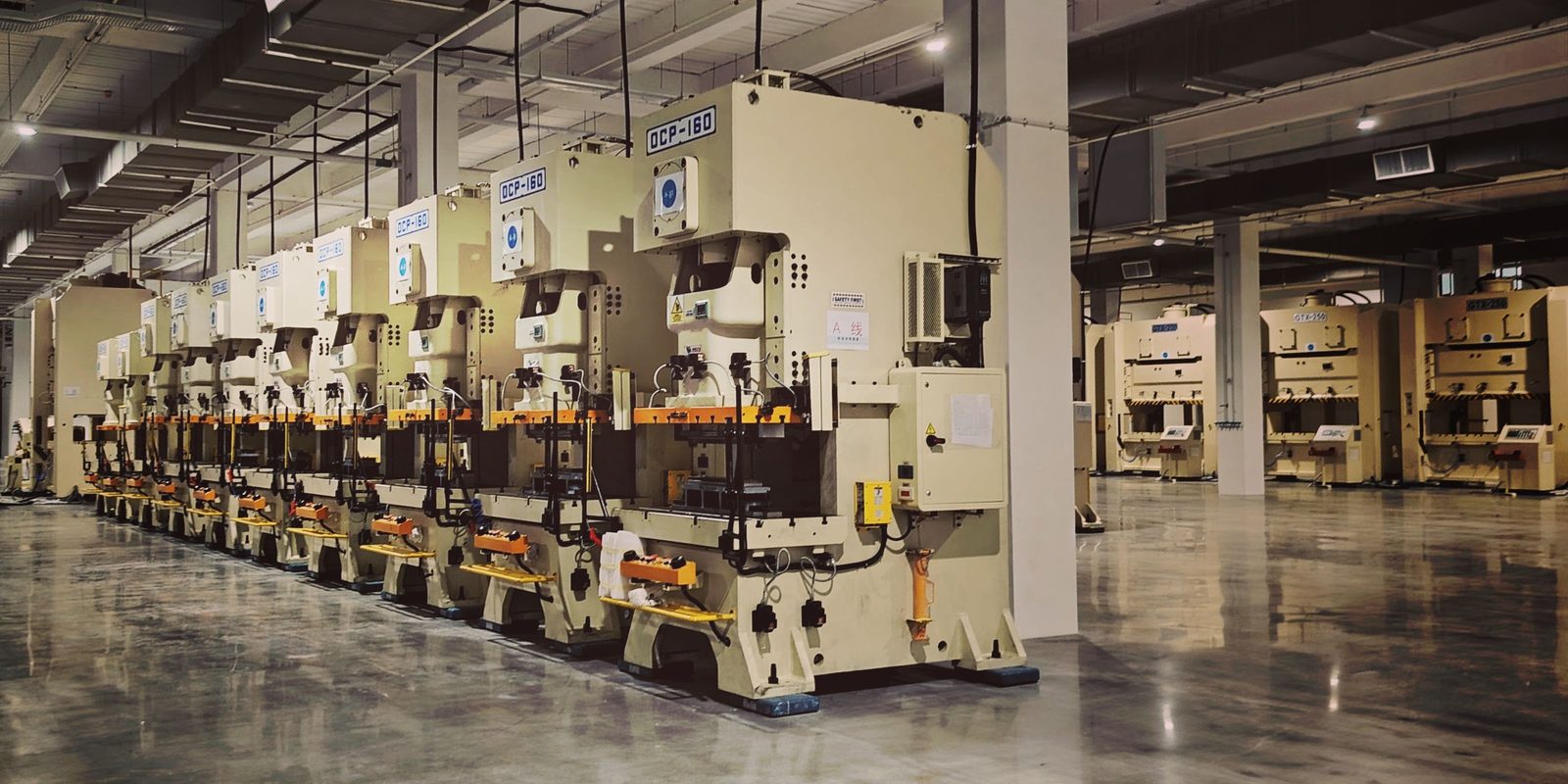 A row of identical stamping presses along a clean, polished factory floor