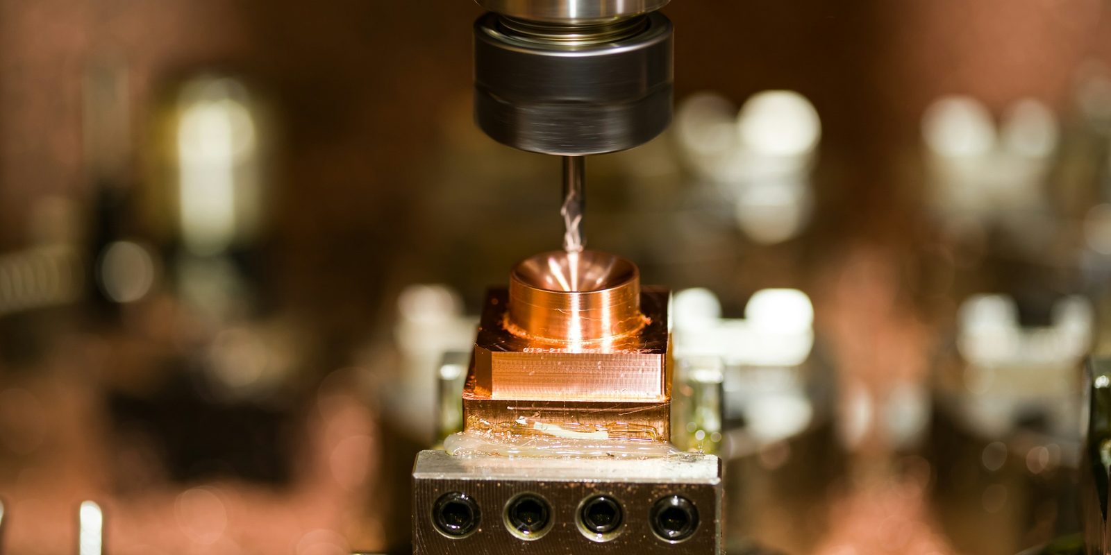 An end mill cutting a copper block clamped in a vise on a milling machine