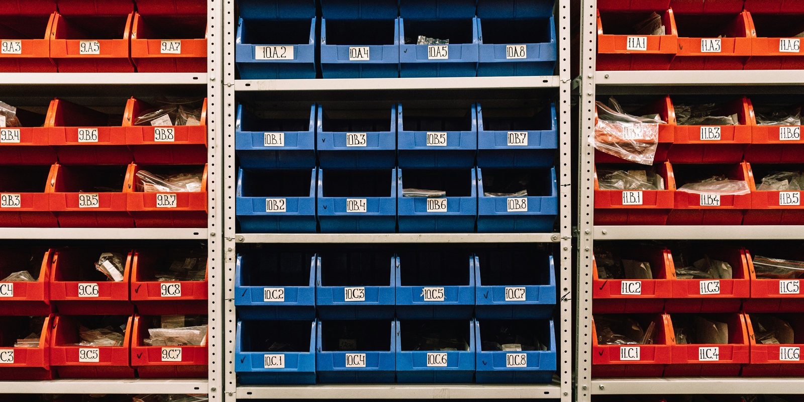 Rows of red and blue parts bins with location labels on steel shelving