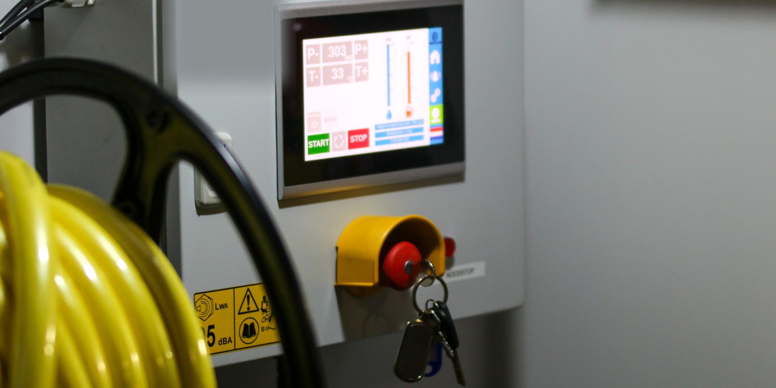 A machine control panel with a touchscreen, a keyed emergency stop and a yellow hose reel in front