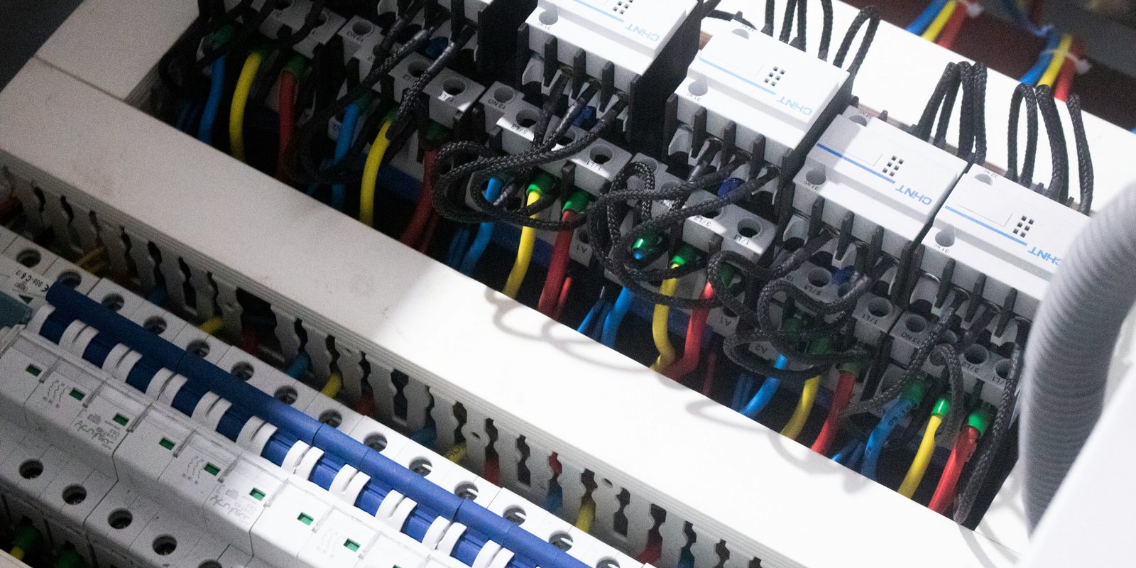 Inside an electrical enclosure: rows of contactors and circuit breakers with colour-coded wiring in white cable ducts
