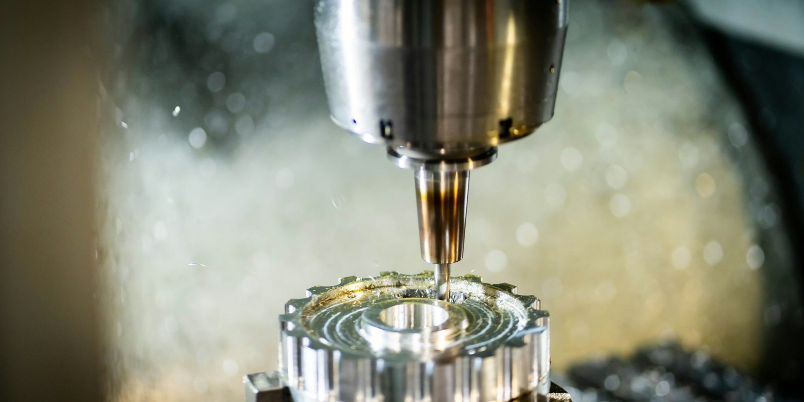 A CNC spindle milling an aluminium gear blank in a bright mist of coolant