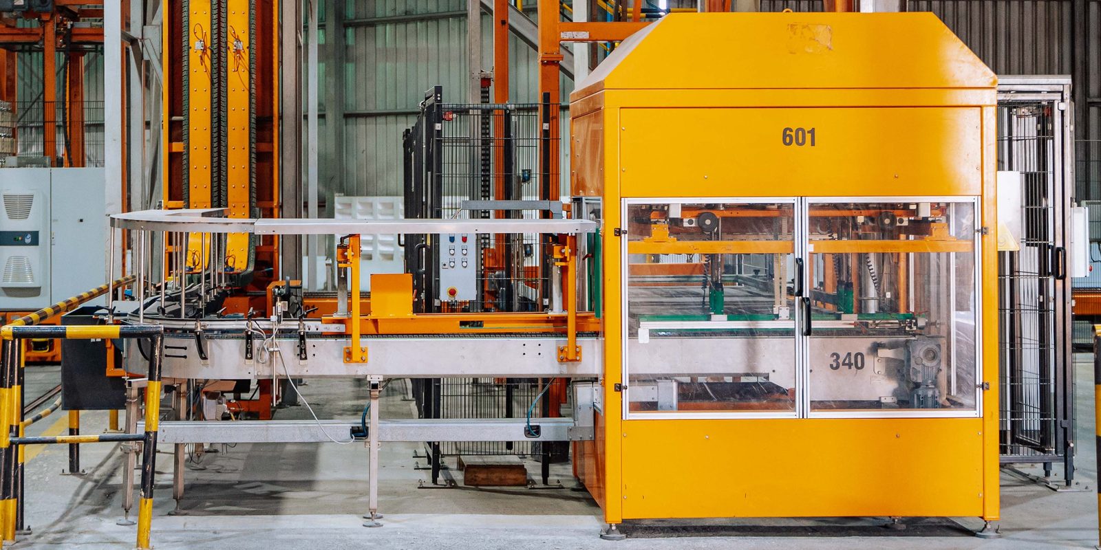 An orange automated packing cell and its conveyor on a clean factory floor marked with yellow lines