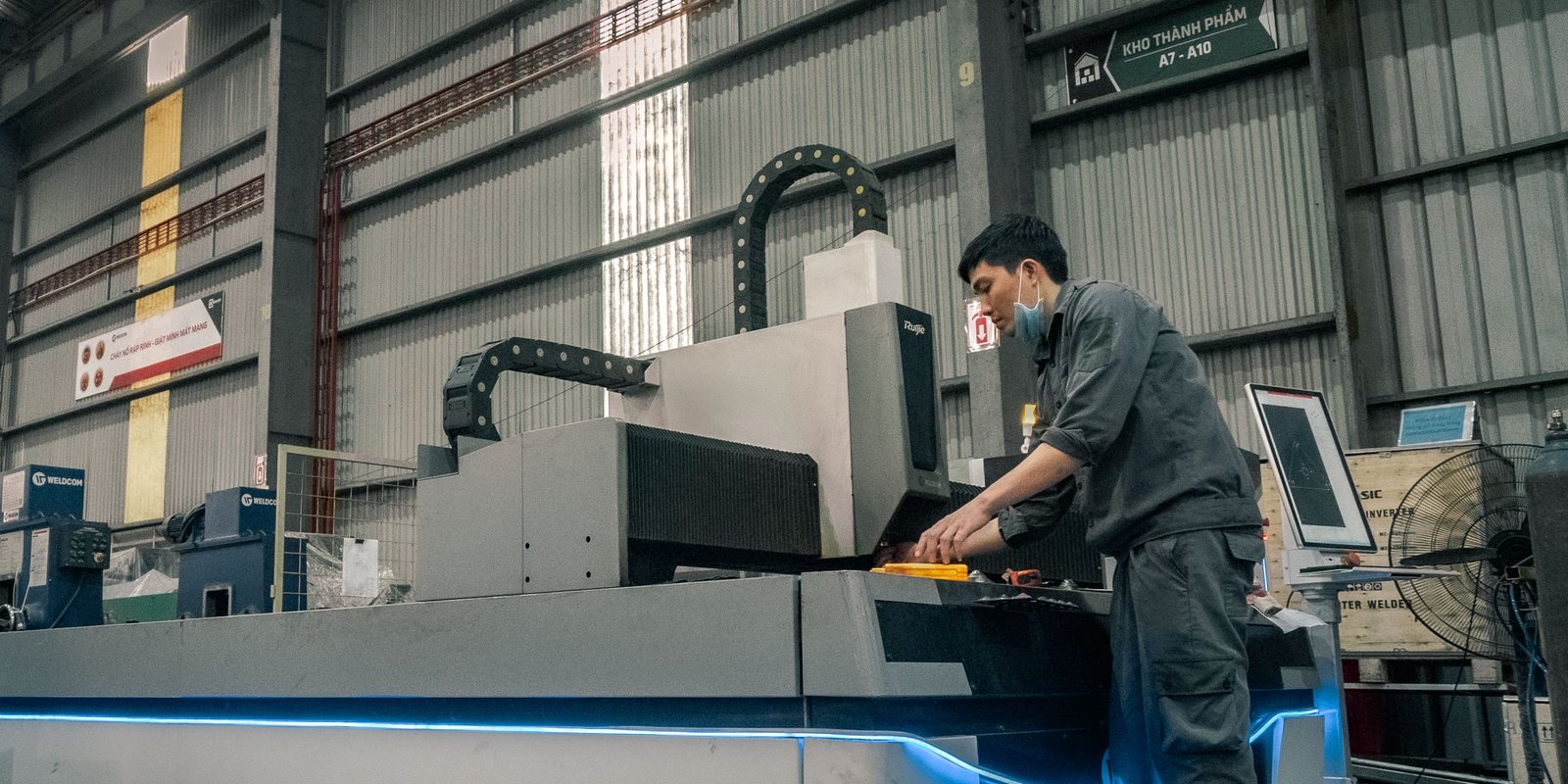 An operator loads a large fibre laser cutting machine with a blue light strip in a spacious factory hall